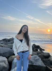 A woman smiles while standing in front of a sunset. 